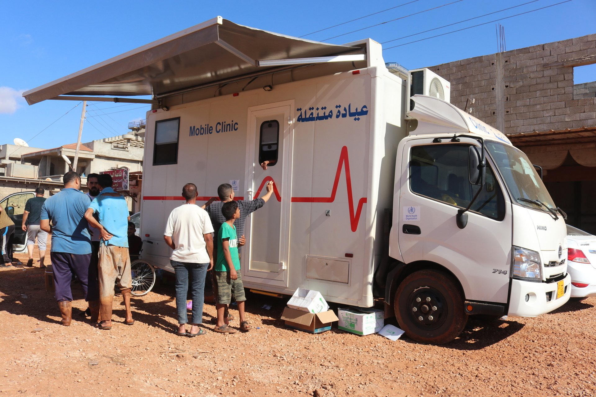 A group of people stand in front of a WHO mobile clinic