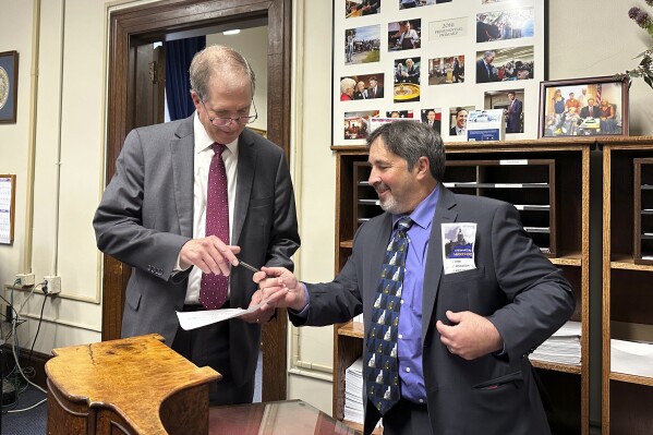 Mark Stewart Greenstein, right, hands a pen back to New Hampshire Secretary of State David Scanlan after filing to get on the state's 2024 Democratic presidential primary ballot on Wednesday, Oct. 11, 2023 in Concord, N.H. Greenstein, of West Hartford, Connecticut, is making his fourth long-shot bid for the nomination. (AP Photo/Holly Ramer)