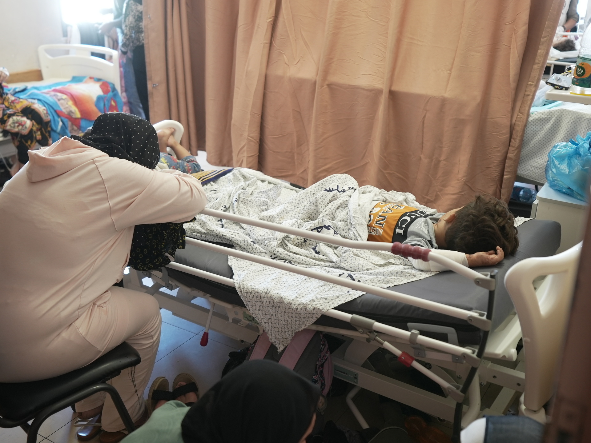 Woman with her head on her arms leaning over a hospital bed on which a child is laying.