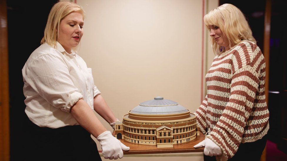 Two female archivists carry a model of the Royal Albert Hall
