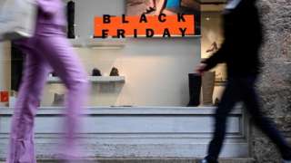 Two people walk past a sign for Black Friday in France.