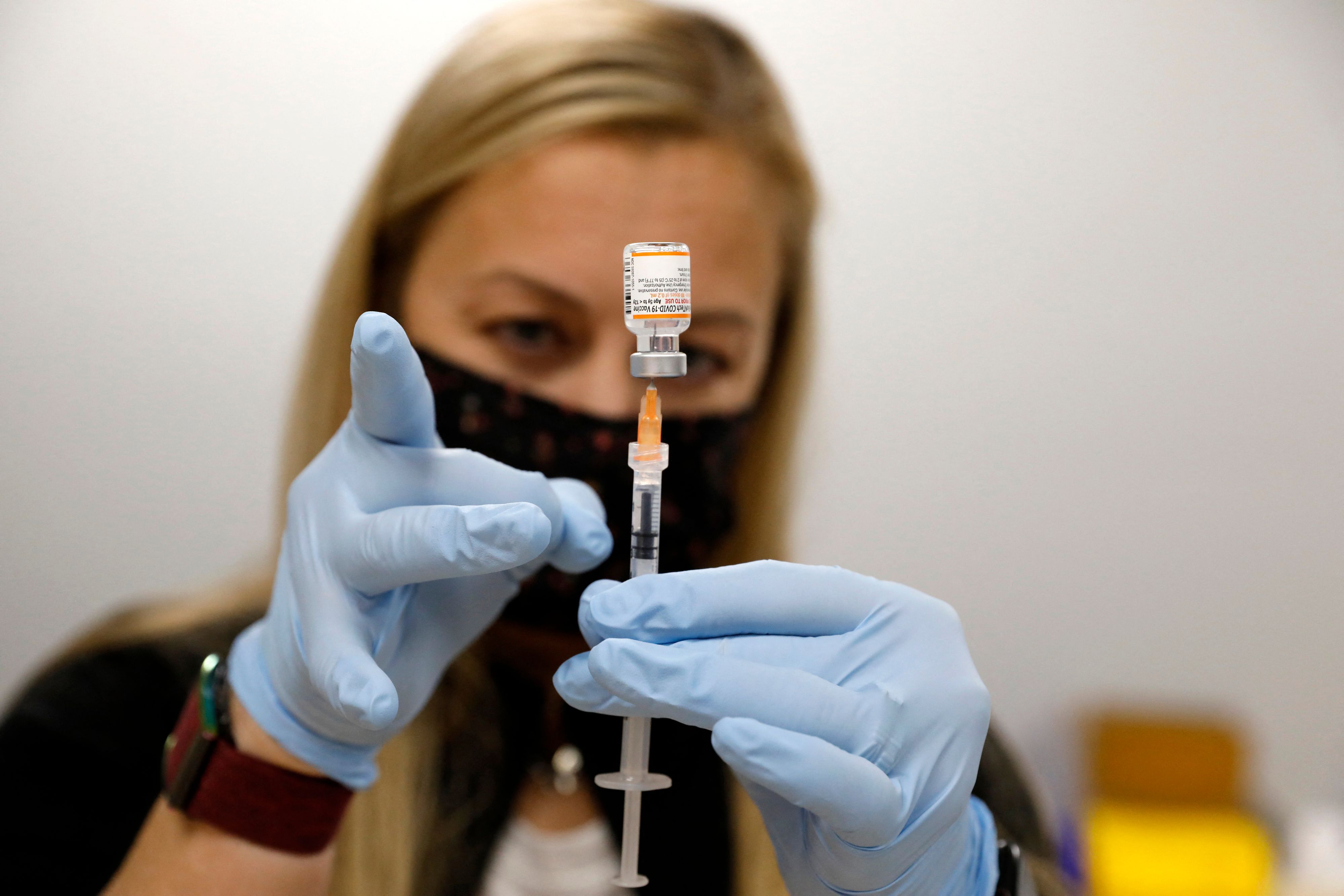 A nurse practitioner wearing a face mask and gloves fills a syringe with the Pfizer Covid-19 vaccine.