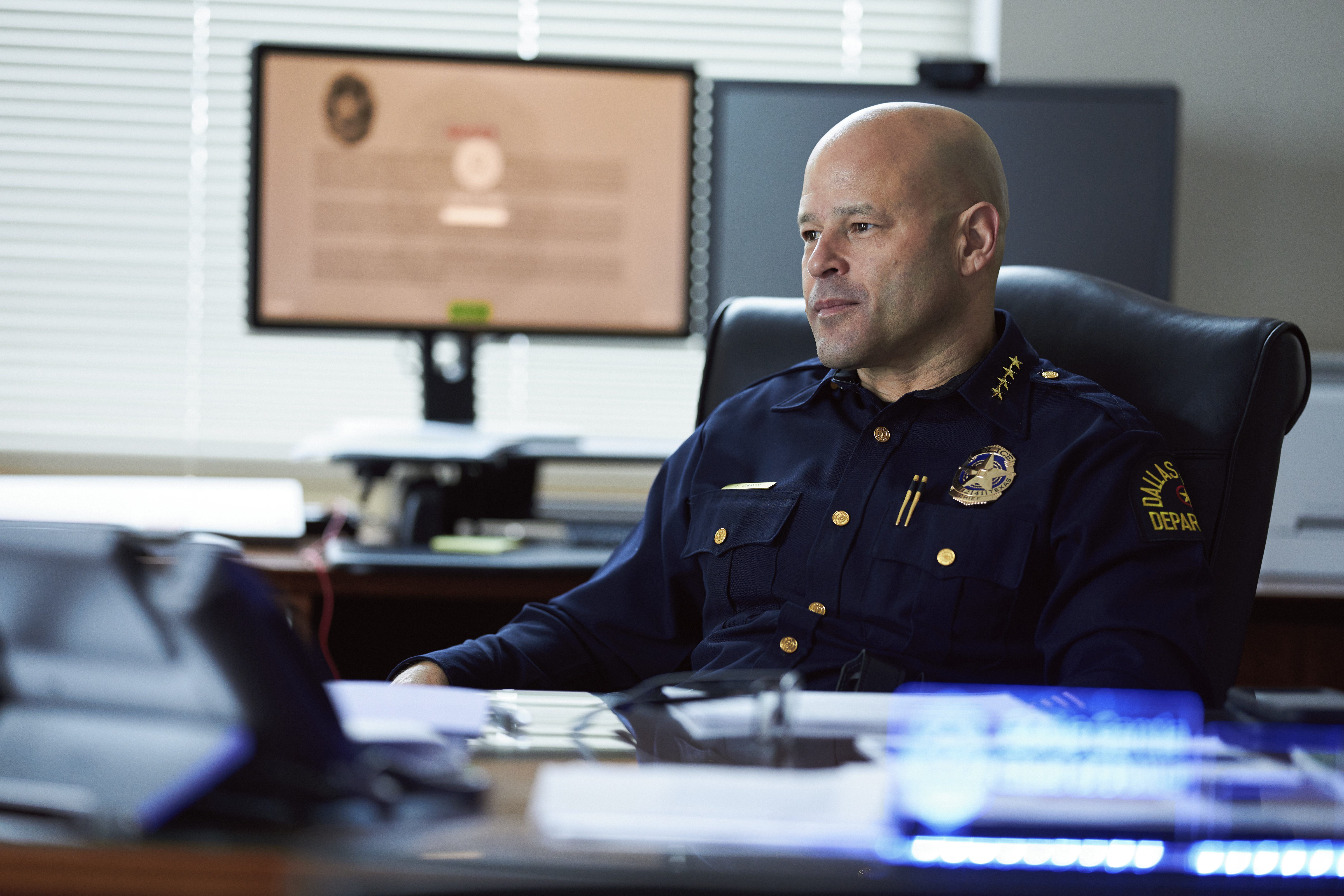 Chief Eddie Garcia, wearing a navy police uniform, sits at his desk with multiple computer monitors in the background.