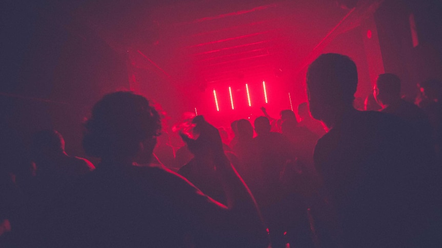 Silhouettes of people dancing in a nightclub bathed in red light.
