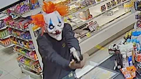 Man holding gun wearing clown mask