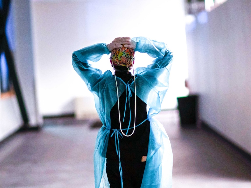 A woman in scrubs walking down a hallway with her hands on her head