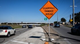 An orange sign at a fork in the road indicates guardrail damage ahead