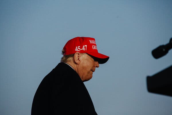 Donald J. Trump in a red cap outdoors in profile. 