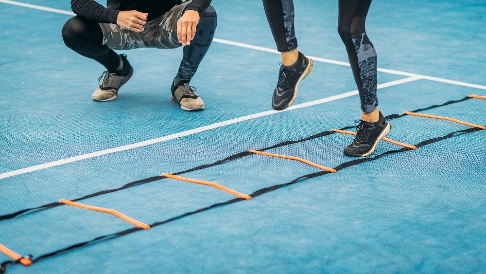 A person exercises using an agility ladder while a coach squats down beside the ladder in piece about agile marketing.