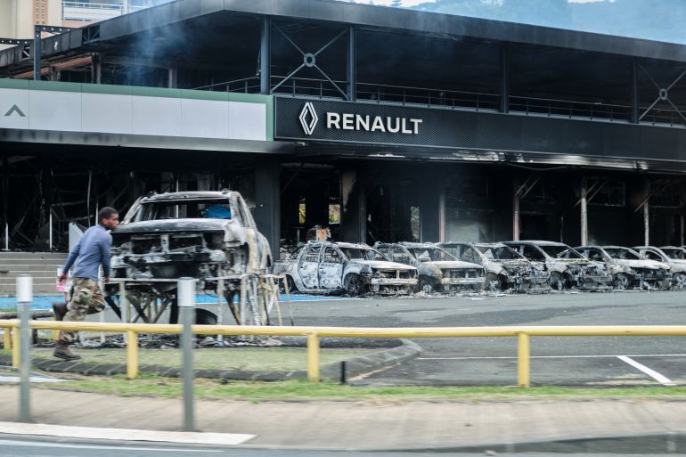 A burned out car showroom in Noumea. Cars parked outside have been burned. A man is