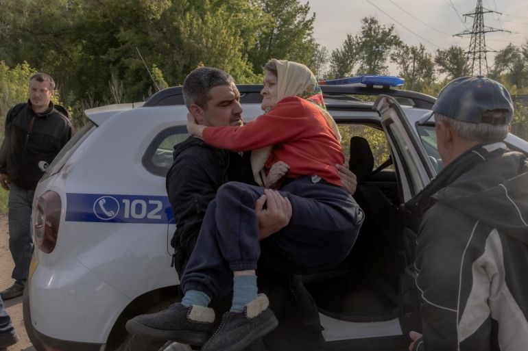 A man carries an elderly woman out of a police car, after she was evacuated from the frontline village of Lyptsi, at a checkpoint, outside Kharkiv, on May 13, 2024, amid the Russian invasion of Ukraine. - Russia on May 13, 2024 pummelled towns and villages in Ukraine's northeastern Kharkiv region days after launching a surprise ground offensive over the border, forcing thousands to evacuate. (Photo by Roman PILIPEY / AFP)