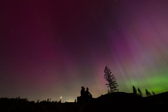 In this image taken with a long exposure, people look at the night sky towards the northern lights, or Aurora Borealis, on Friday, May 10, 2024, in Estacada, Ore