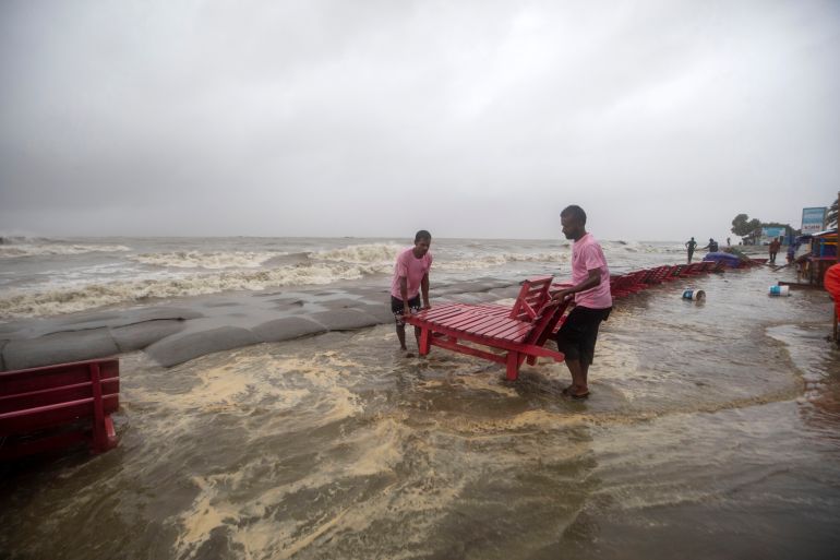 Men salvage a reclining chair and other material as water flows on to the Kuakata beach on the coast of Bay of Bengal caused by the advancing Cyclone Remal in Barisal, Bangladesh