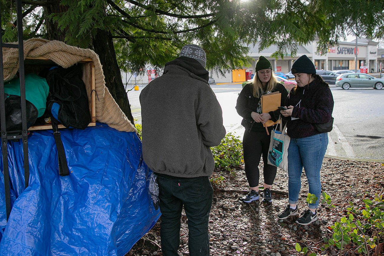 Liz Skinner, right, and Emma Titterness, both from Domestic Violence Services of Snohomish County, speak with a man near the Silver Lake Safeway while conducting a point-in-time count Tuesday, Jan. 23, 2024, in Everett, Washington. The man, who had slept at that location the previous night, was provided some food and a warming kit after participating in the PIT survey. (Ryan Berry / The Herald)