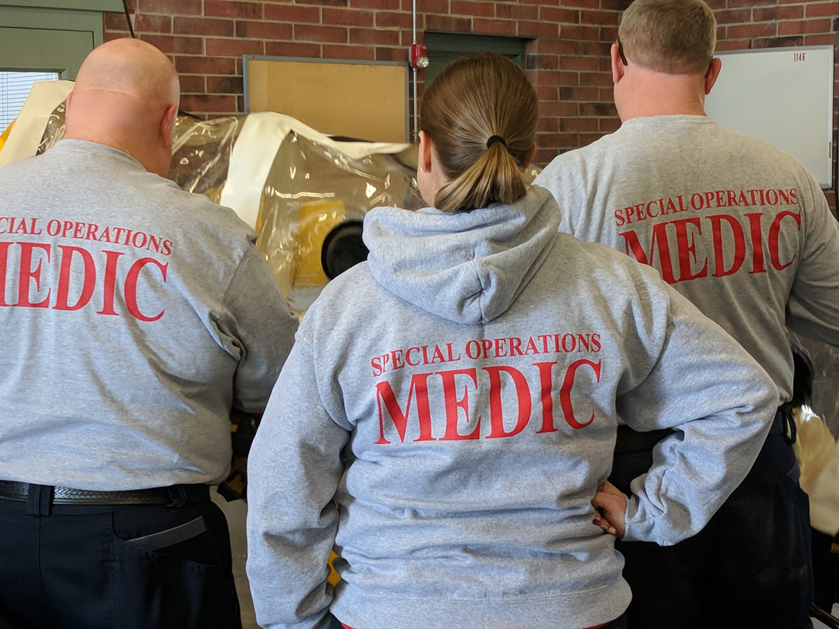 Emergency medical personnel with their backs to the camera showing logos of the MED-ACT department.