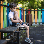 Child sitting alone on a playground bench.