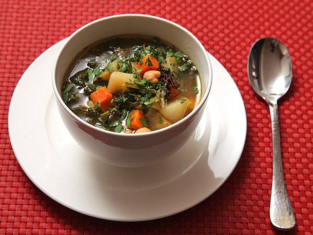 A bowl of hearty winter vegetable soup, served on a plate atop as red woven placemat.