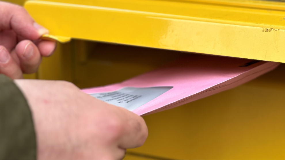 Person wirft roten Wahlbrief in einen Briefkasten