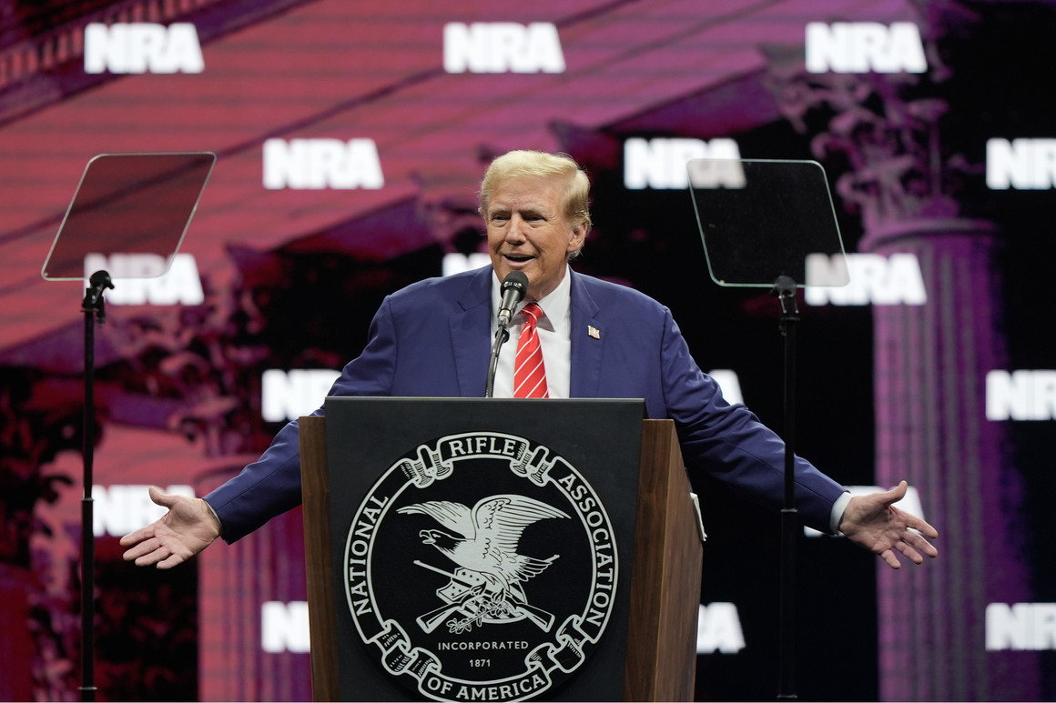 Donald Trump gestures at a podium with the National Rifle Association's seal.