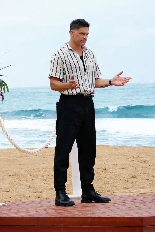 A person in a striped shirt and black pants stands on a platform on a beach and gestures