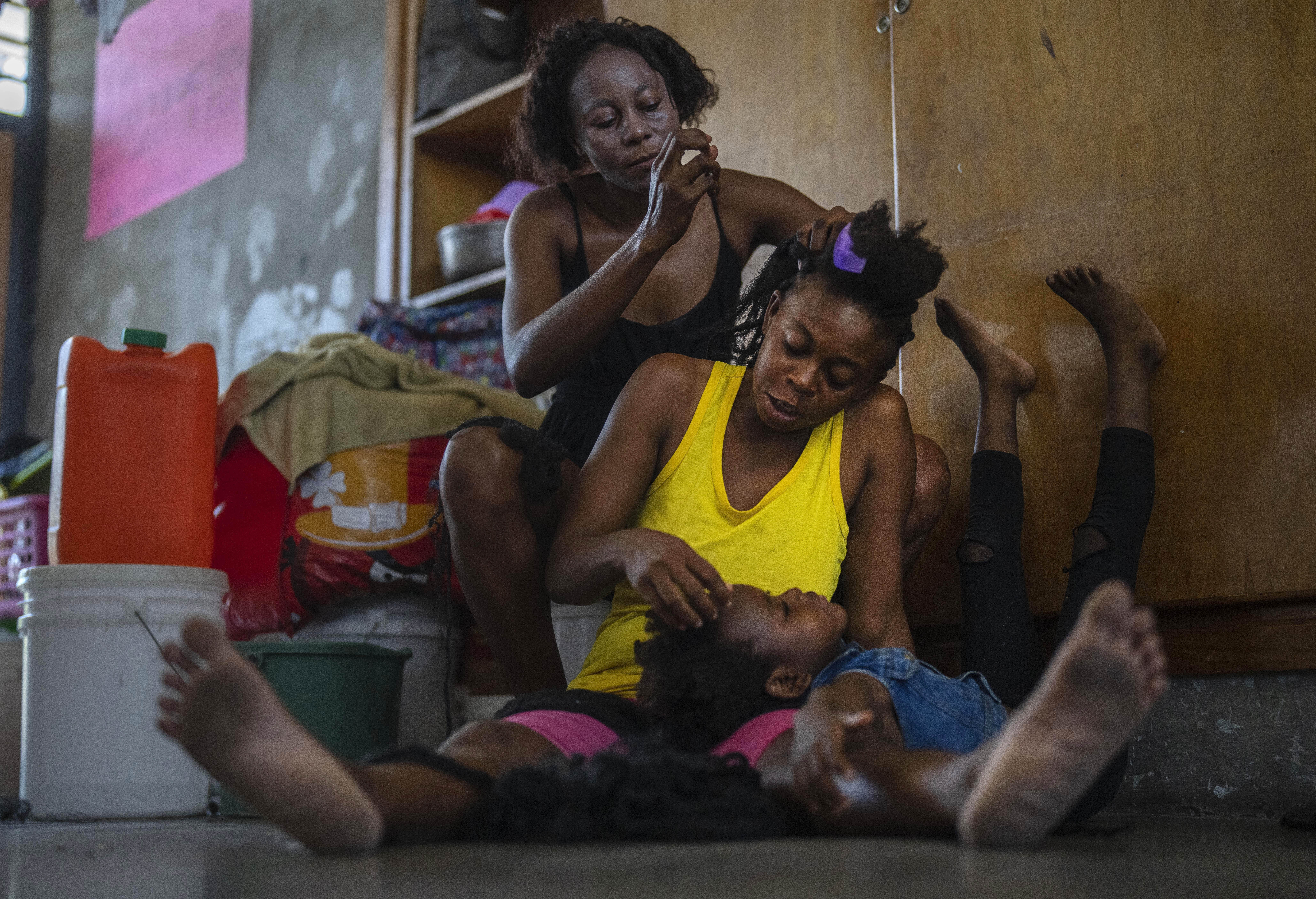A child rests her head on the lap of her mother as she gets her hair done, at a school turned into a makeshift shelter for people displaced by gang violence, in Port-au-Prince, Haiti, Wednesday, May 8, 2024. (AP Photo/Ramon Espinosa)