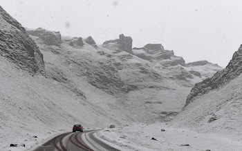 A car is driven on a snow-covered road as it passes through Winnats Pass near Castleton, central England 