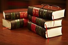 Stacks of law books on a wood table with eyeglasses