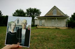 Photo of Grant Wood's Painting &quot;American Gothic&quot; Held up in Front of the Gothic Revival House in Disrepair