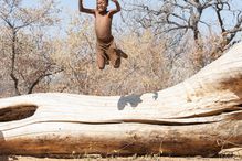 San (Bushman) child jumping of fallen tree. Grashoek, Bushmanland , Namibia