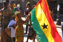 Young girl holding the flag of Ghana in a crowd of people on a sunny day.