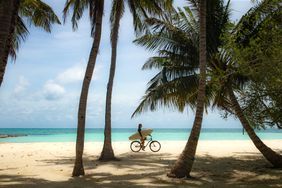 A girl rides a bicycle on a tropical island in search of surf