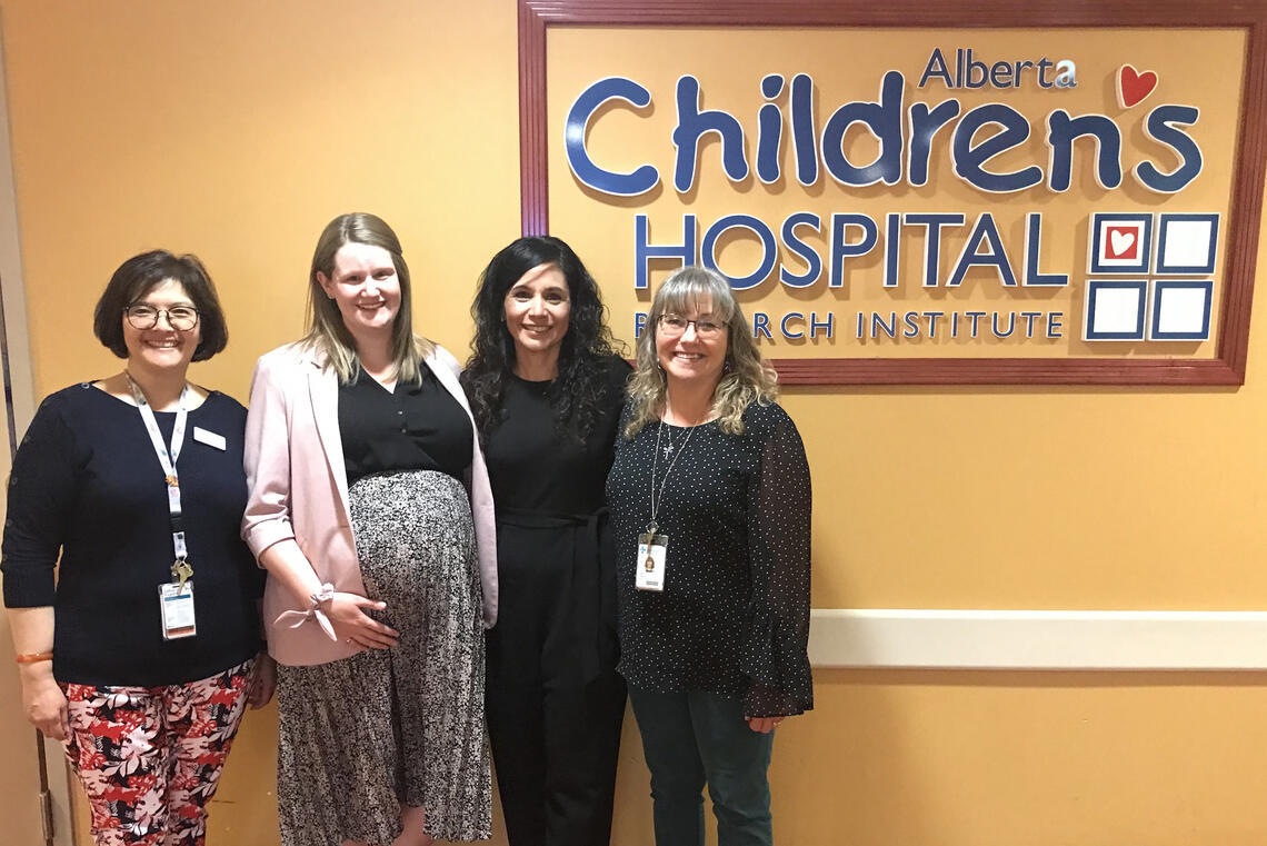 A group of women in stand in front of the Alberta Children's Hospital Sign