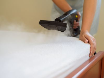 A person using a steam generator to clean a bed