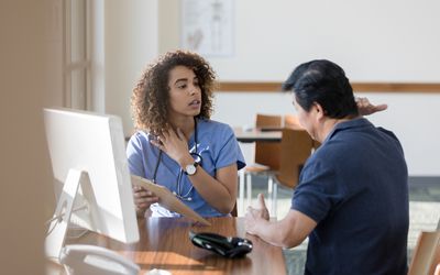 Serious female doctor asks a senior man about his symptoms. She is gesturing toward her neck while talking with the man. - stock photo