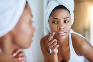 young woman inspecting her skin in front of the bathroom mirror and looking upset