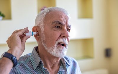 Closeup view at an elderly person using a bottle of eardrops due to ear problems
