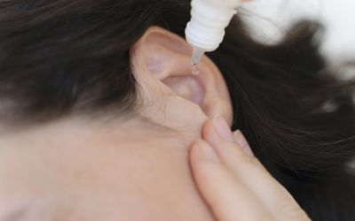 Close up shot of a person holding a dropper of a clear liquid above a person's ear, administering ear drops