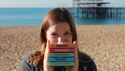 Hazel Reynolds, Founder of Gamely Games, standing in a beach holding all of her games. 