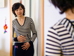 woman early in her pregnancy looking at her clothed tummy in the mirror