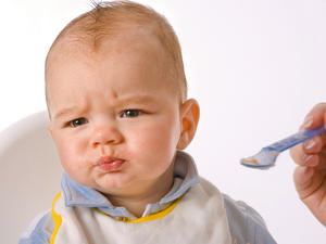 baby in high chair pursing lips shut and turning away from spoon full of pureed food