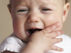 teething baby with fingers in mouth and crying