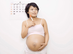 pregnant woman standing in front of wall calendar and holding a texta