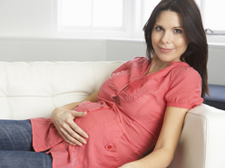woman sitting on a sofa resting her hand on her pregnant belly to feel her baby’s movements
