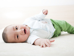smiling baby wearing green pants and rolling over on a white carpet