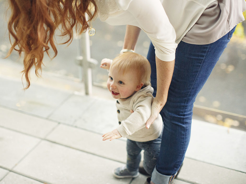 redhead woman holding a baby trying to walk