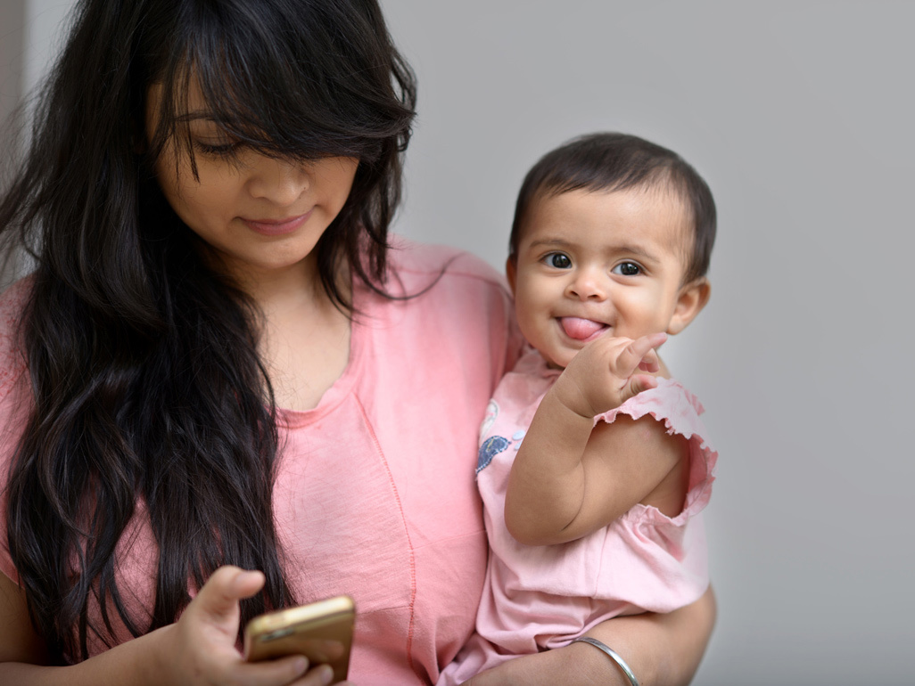 mother holding a baby and looking at her phone