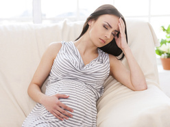 a pregnant woman in pain, resting on the sofa with one hand on her tummy