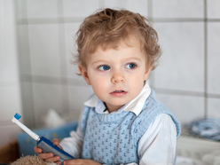 toddler in the bathroom holding an electric toothbrush
