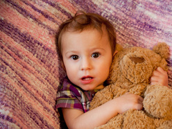 Little girl awake in bed clutching her teddy