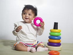 baby holding pink ring from stacking set next to her on the floor